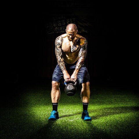 A man is squatting down while holding a kettlebell in his hands.