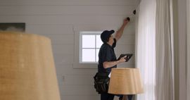 A man is installing a security system in a living room.