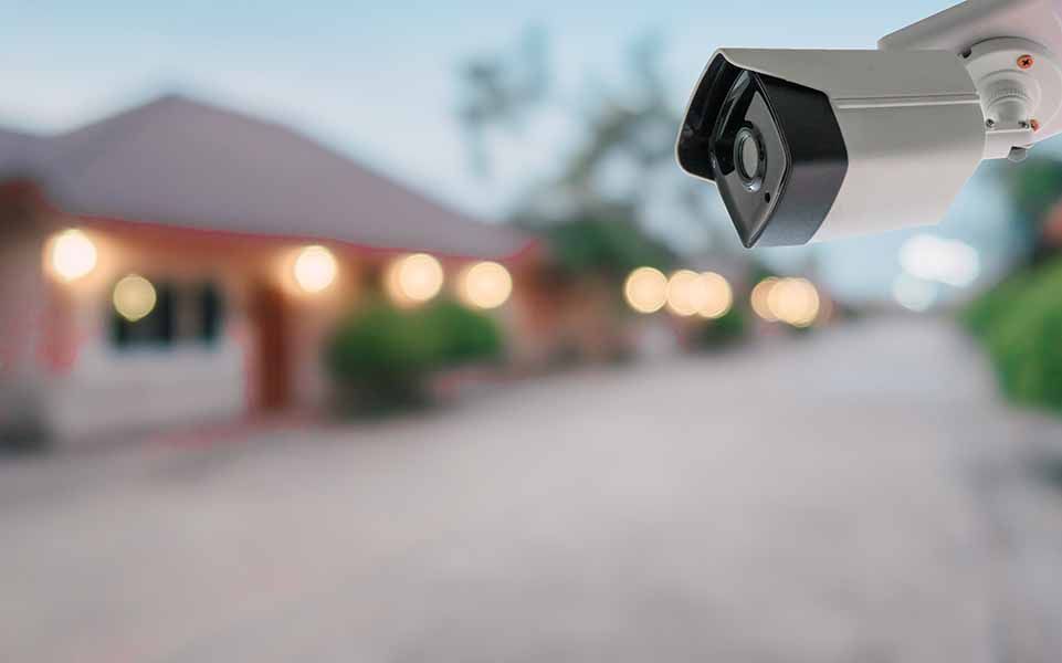 A security camera is hanging from a pole in front of a house.