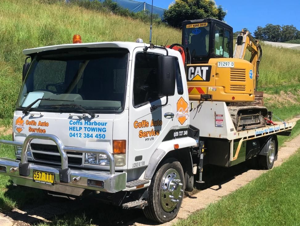 A Tow Truck With a Cat Excavator on the Back is Parked on a Dirt Road — Coffs Tow Trucks In North Boambee Valley, NSW