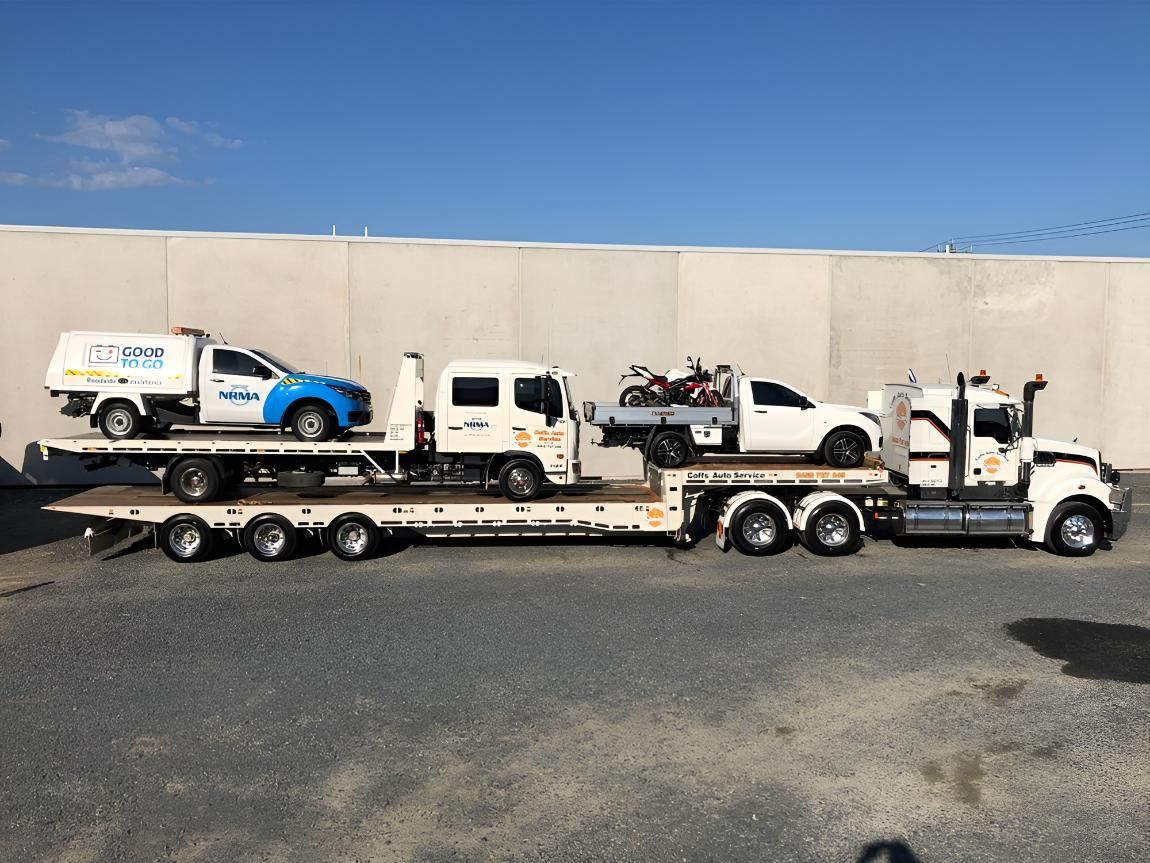 A Tow Truck is Carrying Two Cars and a Motorcycle on a Flatbed Trailer — Coffs Tow Trucks In North Boambee Valley, NSW