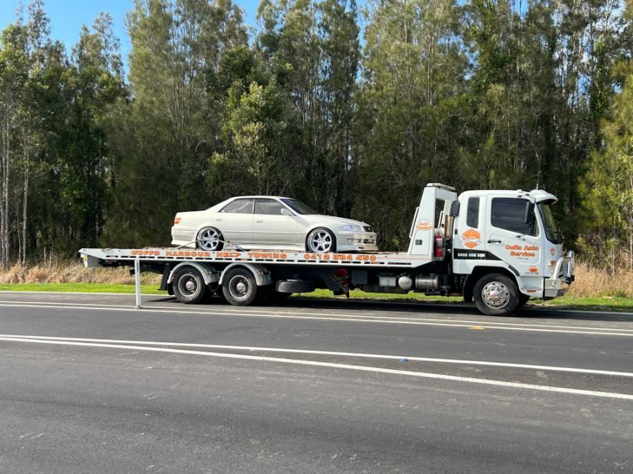 A Tow Truck is Carrying a White Car on the Back of It — Coffs Tow Trucks In Woolgoolga, NSW