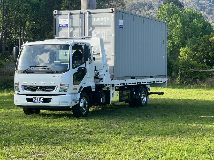 A White Truck With a Container on the Back is Parked in a Grassy Field — Coffs Tow Trucks In Woolgoolga, NSW