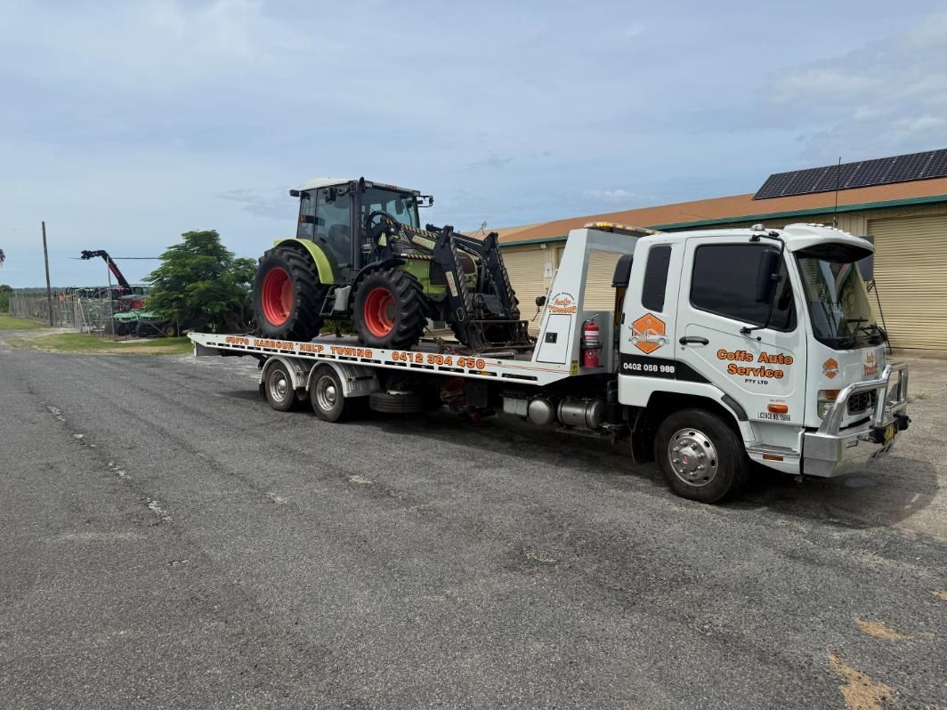 A Tow Truck is Carrying a Tractor on a Flatbed Trailer — Coffs Tow Trucks In Sawtell, NSW