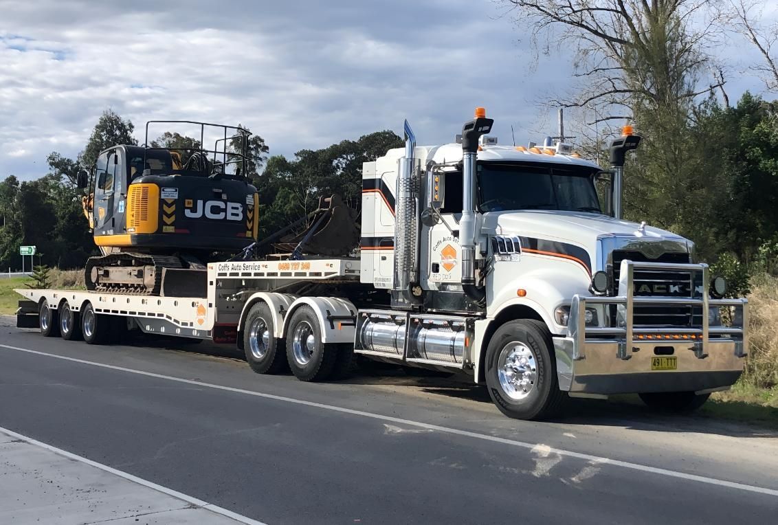 A Semi Truck is Carrying a Jcb Excavator on a Flatbed Trailer — Coffs Tow Trucks In North Boambee Valley, NSW