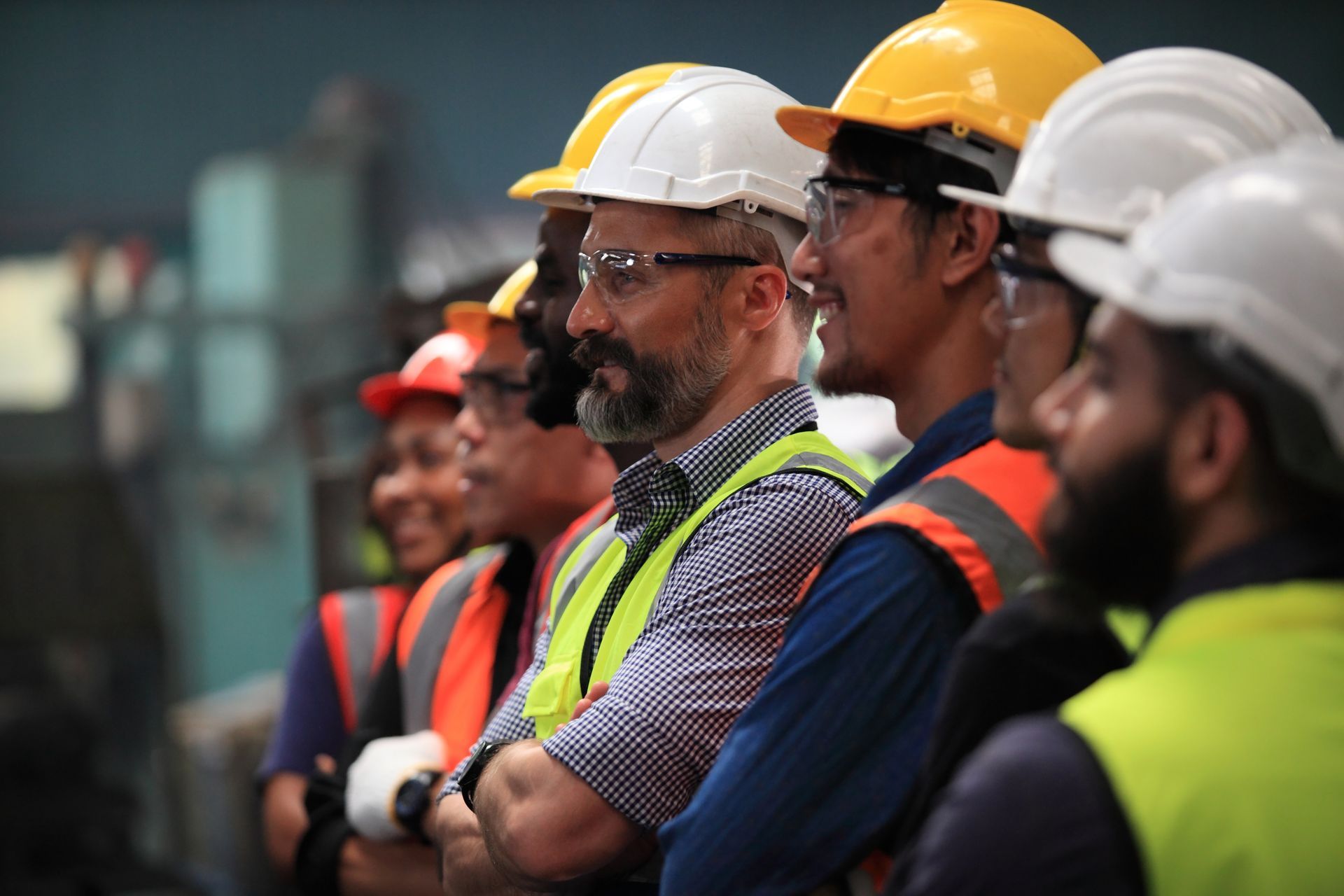A group of construction workers wearing hard hats and safety vests are standing in a line.
