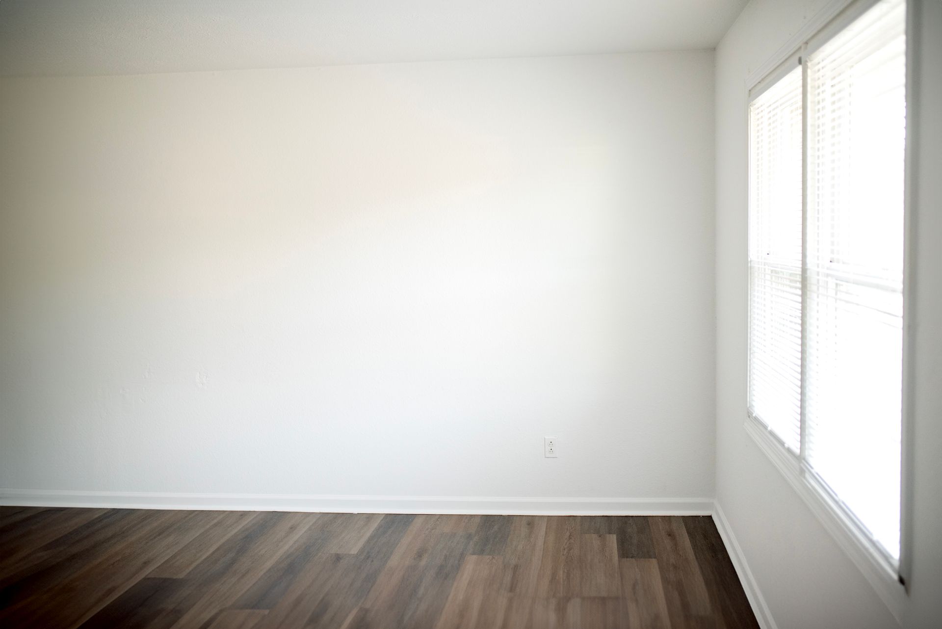 An empty room with hardwood floors , white walls , and two windows.