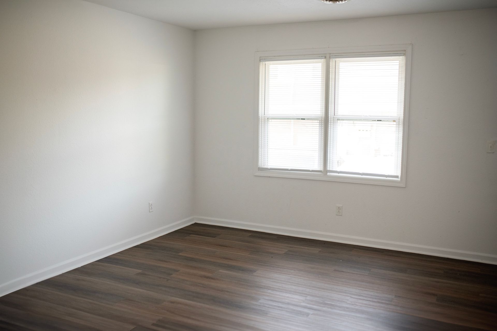 An empty room with hardwood floors and two windows.