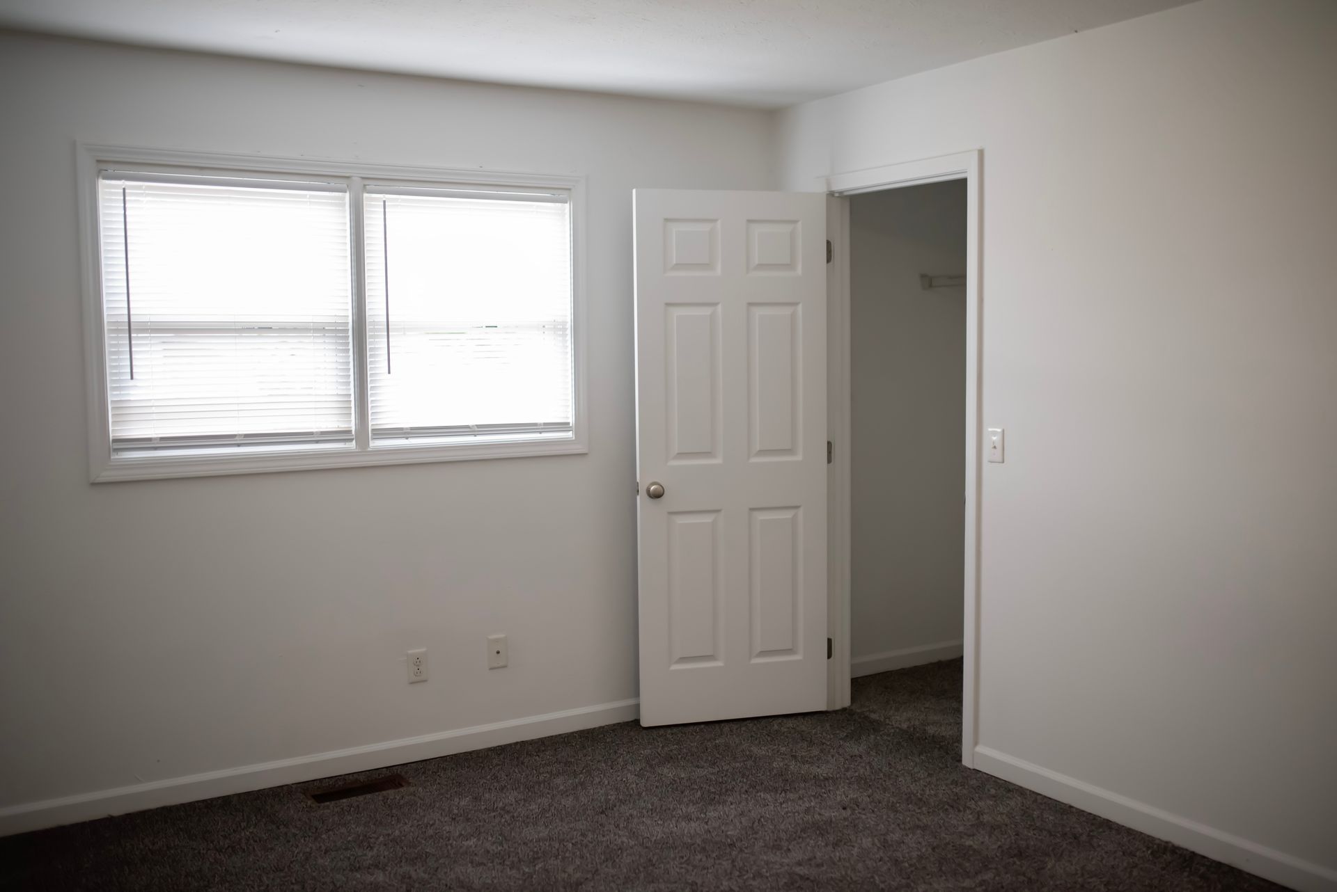 An empty bedroom with a door open and a window.
