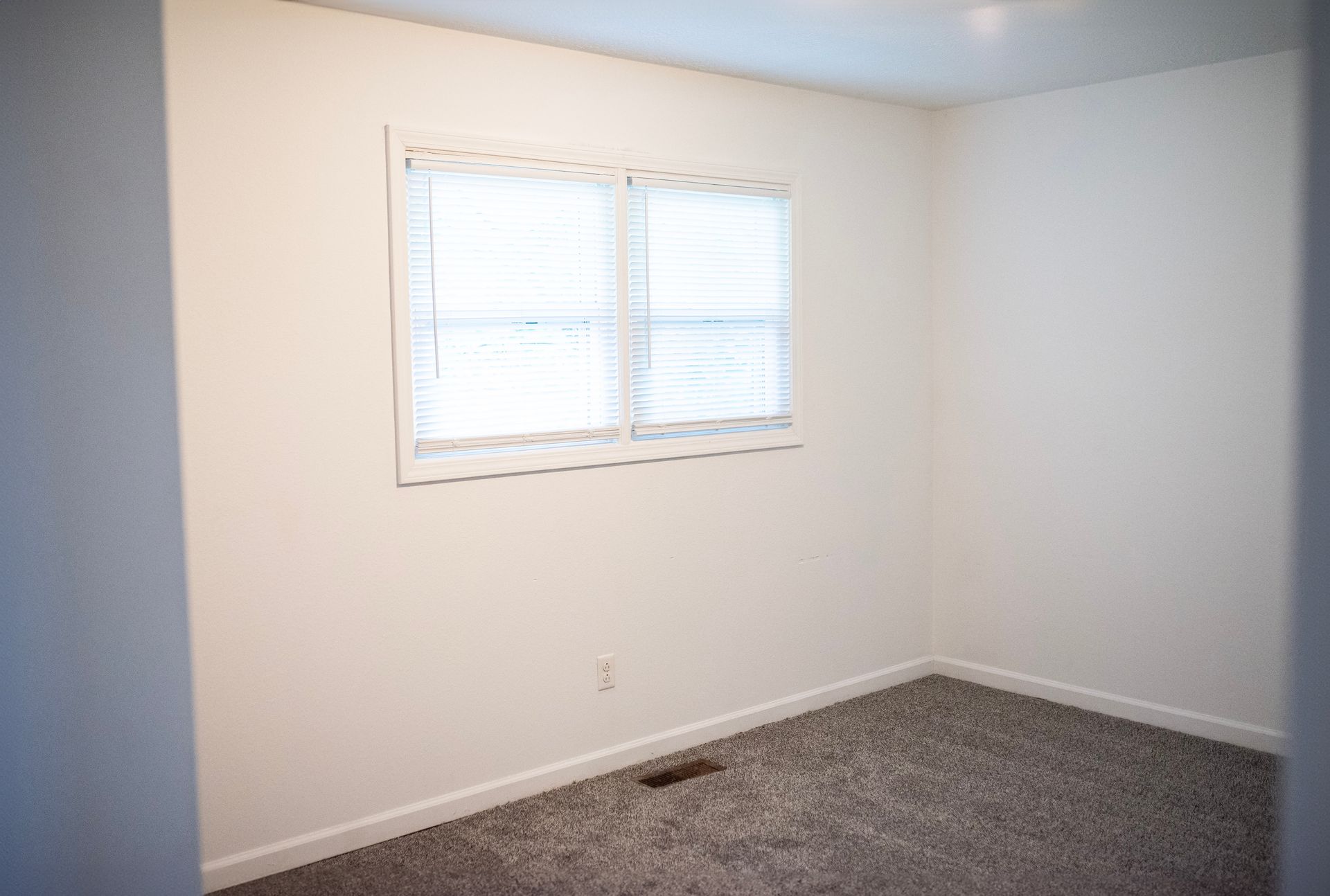 An empty bedroom with a window and a carpeted floor.