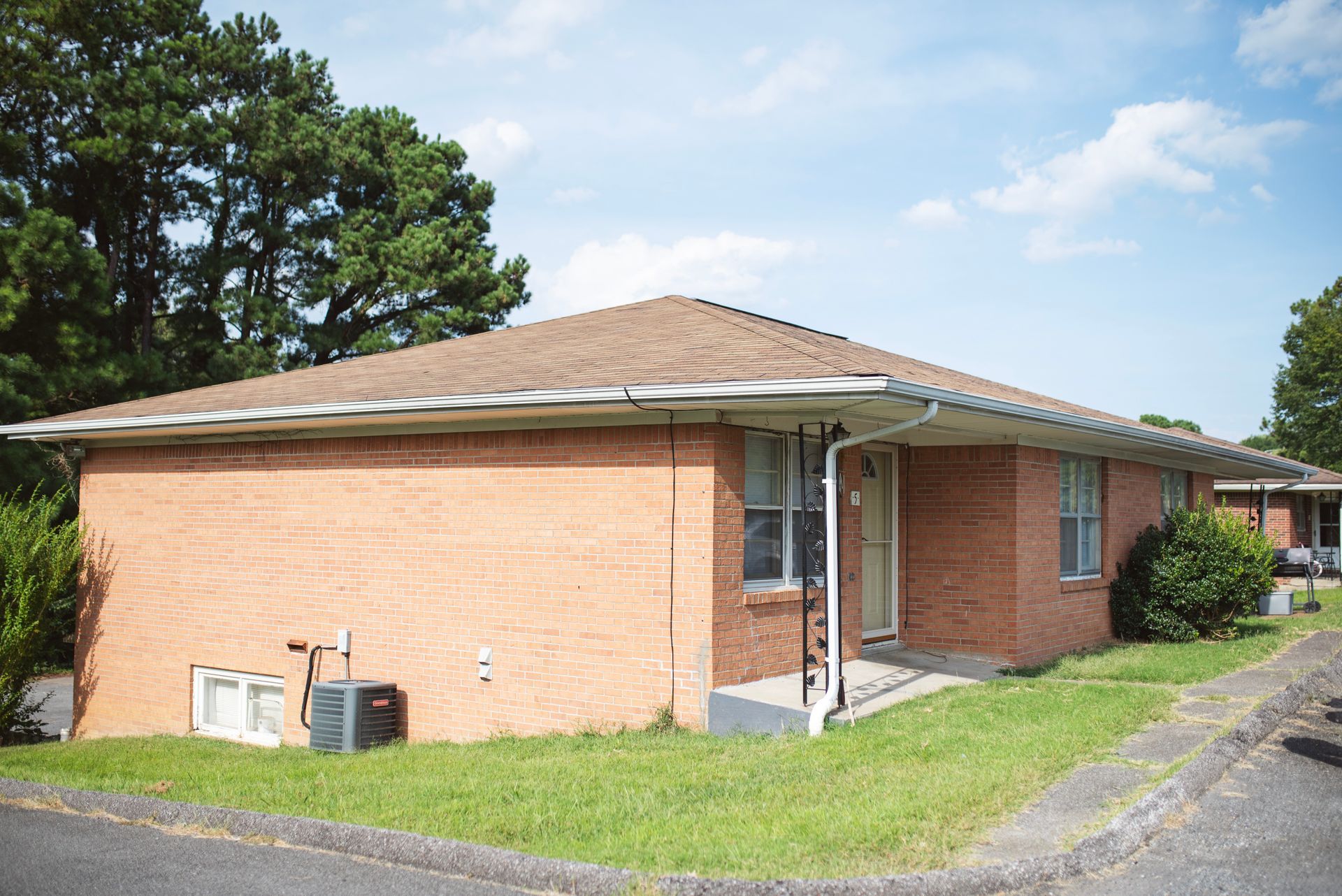 A brick house with a brown roof is sitting on a lush green lawn.
