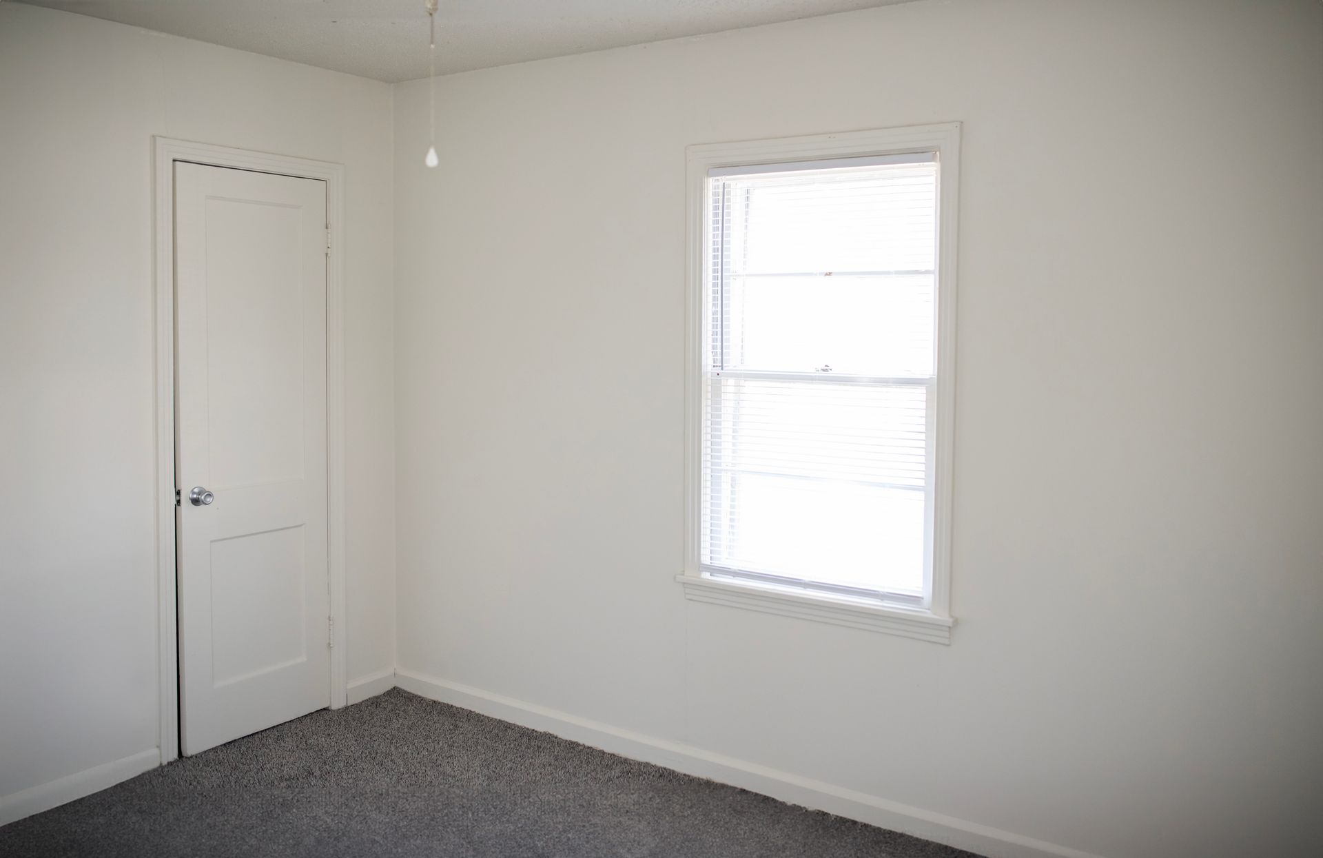 An empty bedroom with a window and a door.