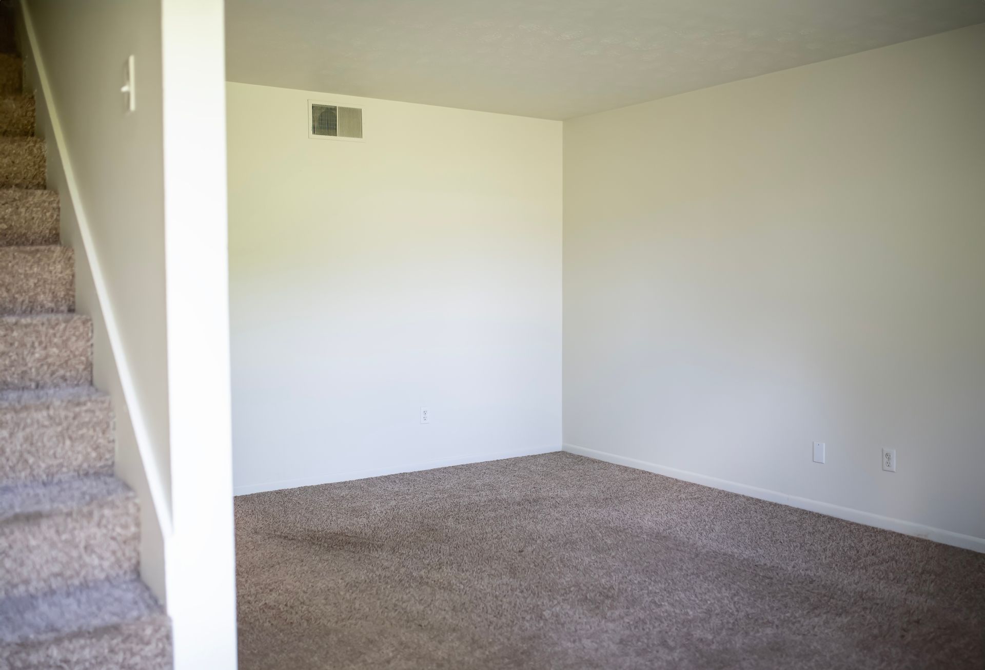 An empty living room with stairs leading up to the second floor.