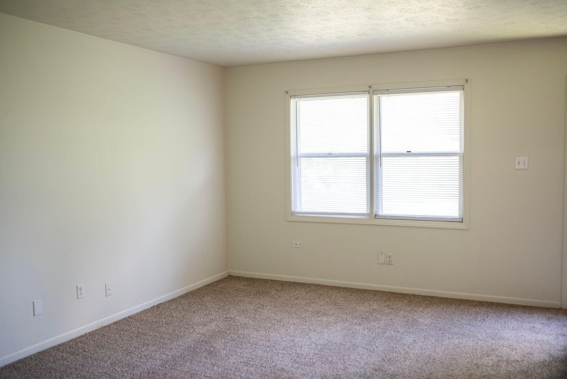 An empty living room with a window and carpet.