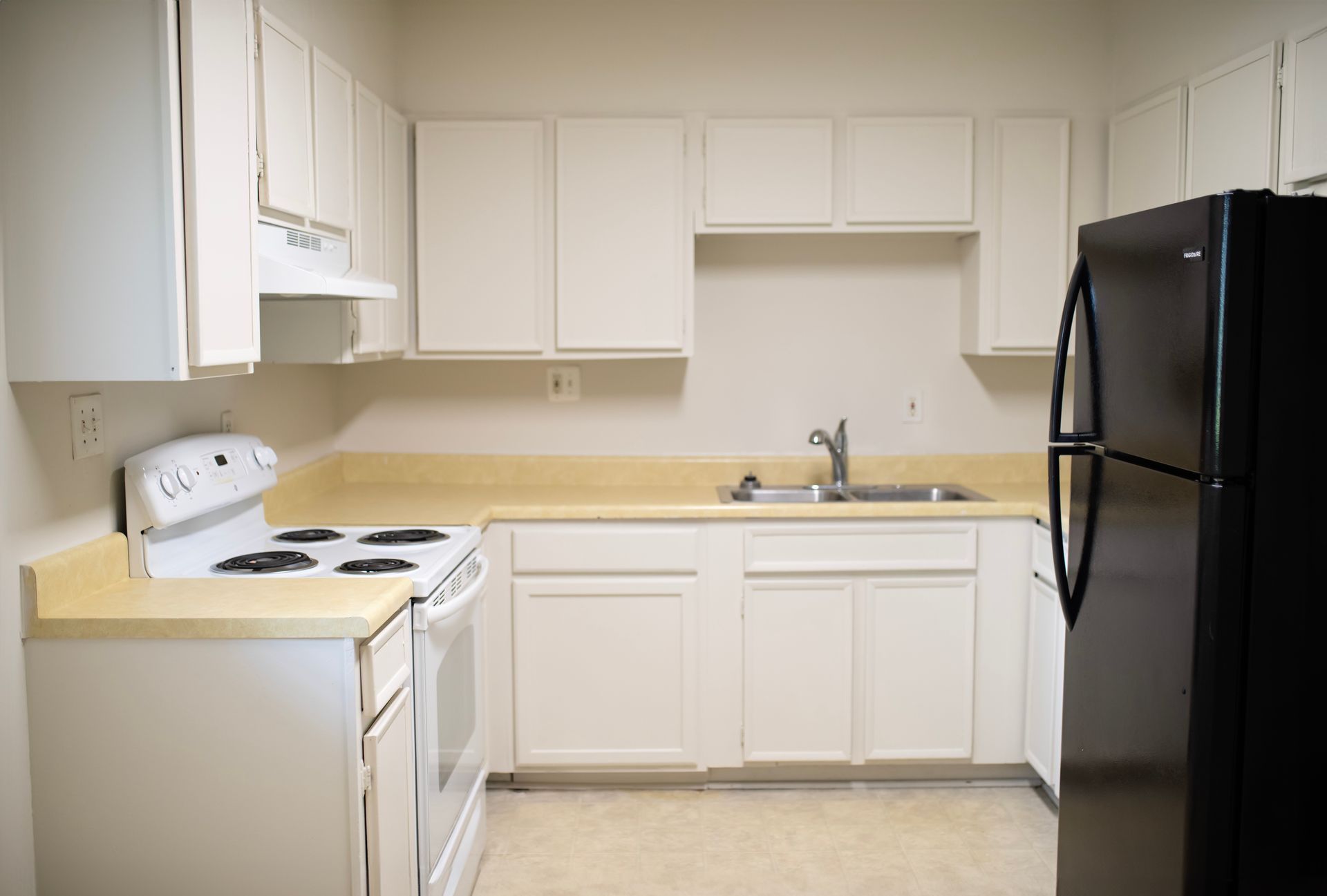 An empty kitchen with white cabinets and a black refrigerator