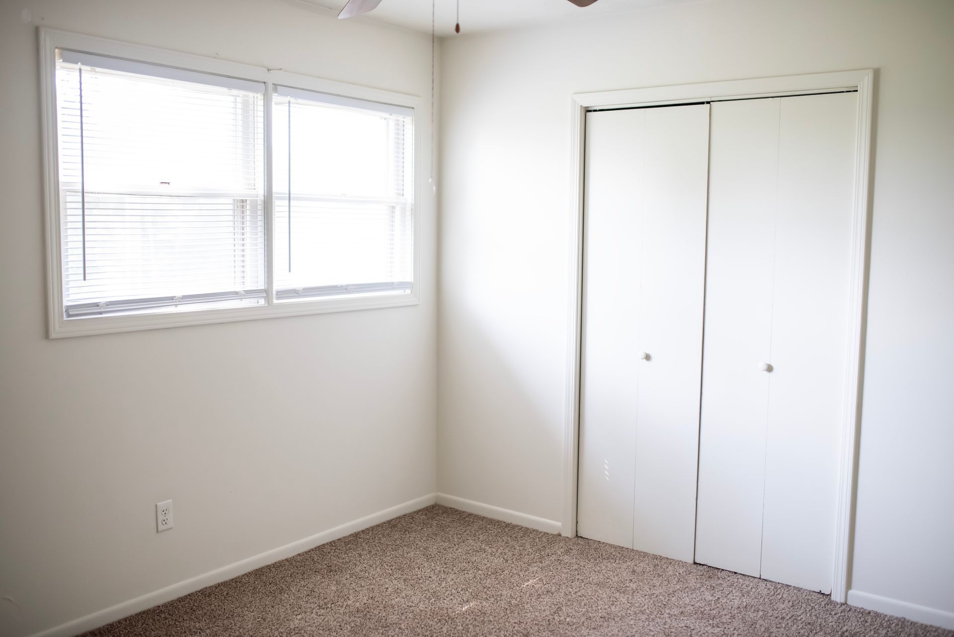 An empty bedroom with a closet and two windows.