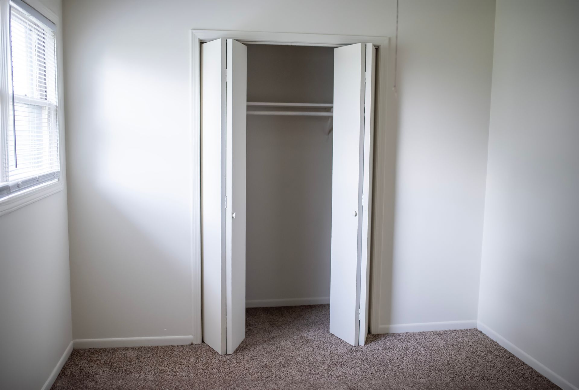 An empty bedroom with a closet and a window.