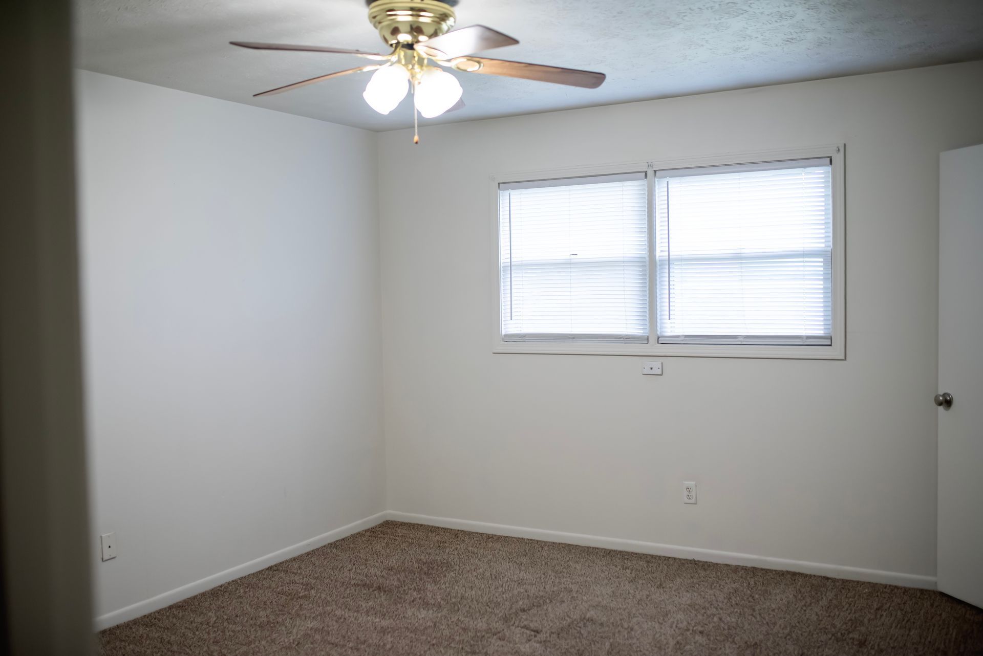 An empty bedroom with a ceiling fan and a window