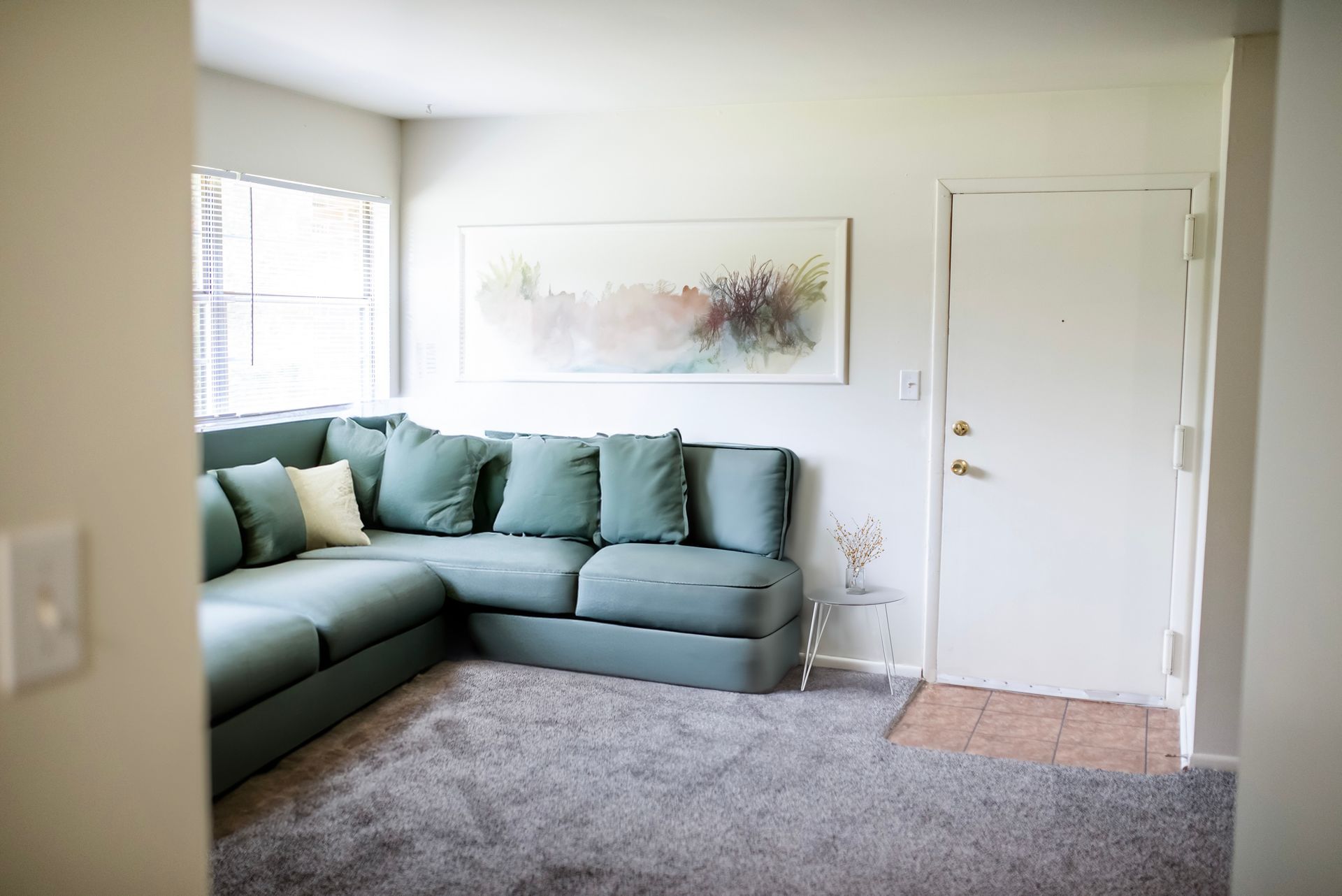 A living room with a green sectional couch and a painting on the wall.