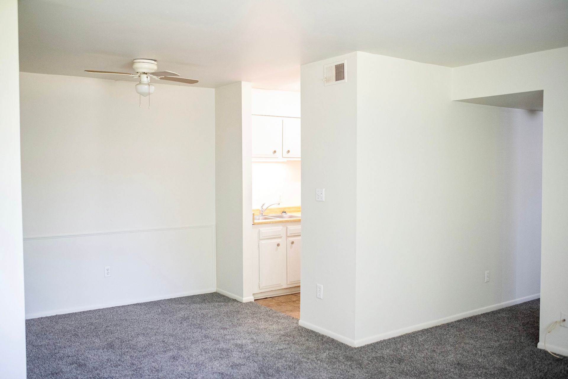 An empty living room with a ceiling fan and a gray carpet.