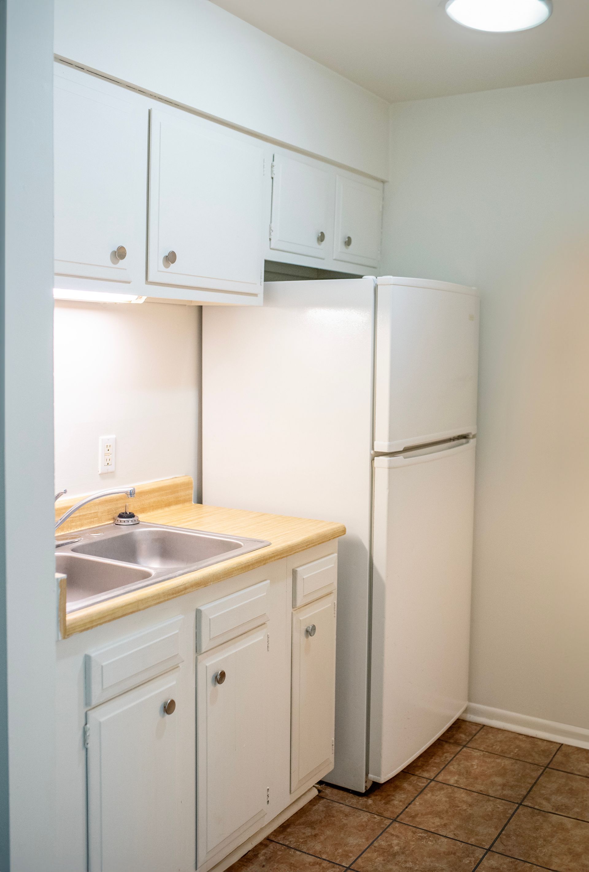 A kitchen with white cabinets , a sink , and a refrigerator.