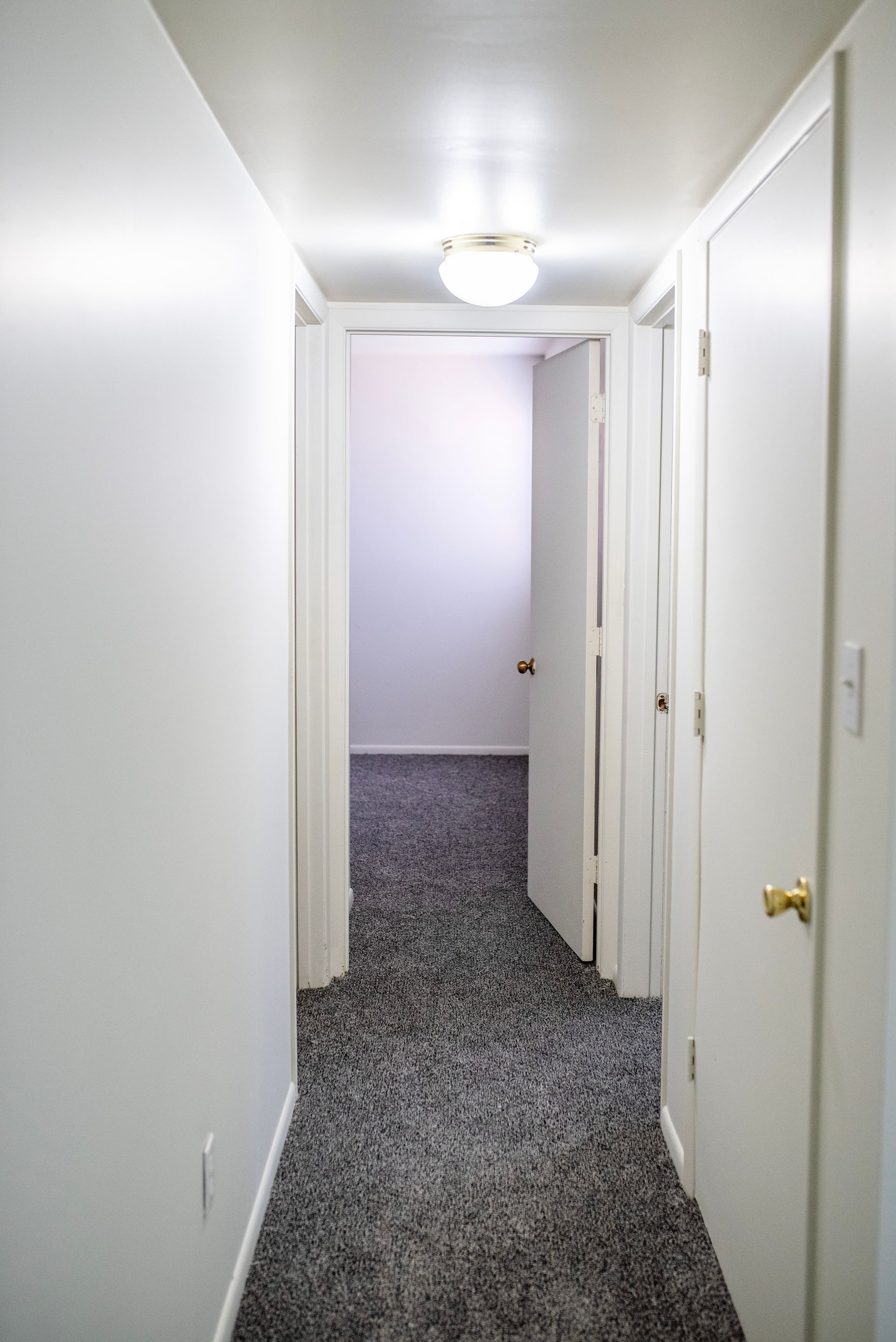 A hallway with a carpeted floor and white walls leading to a bedroom.