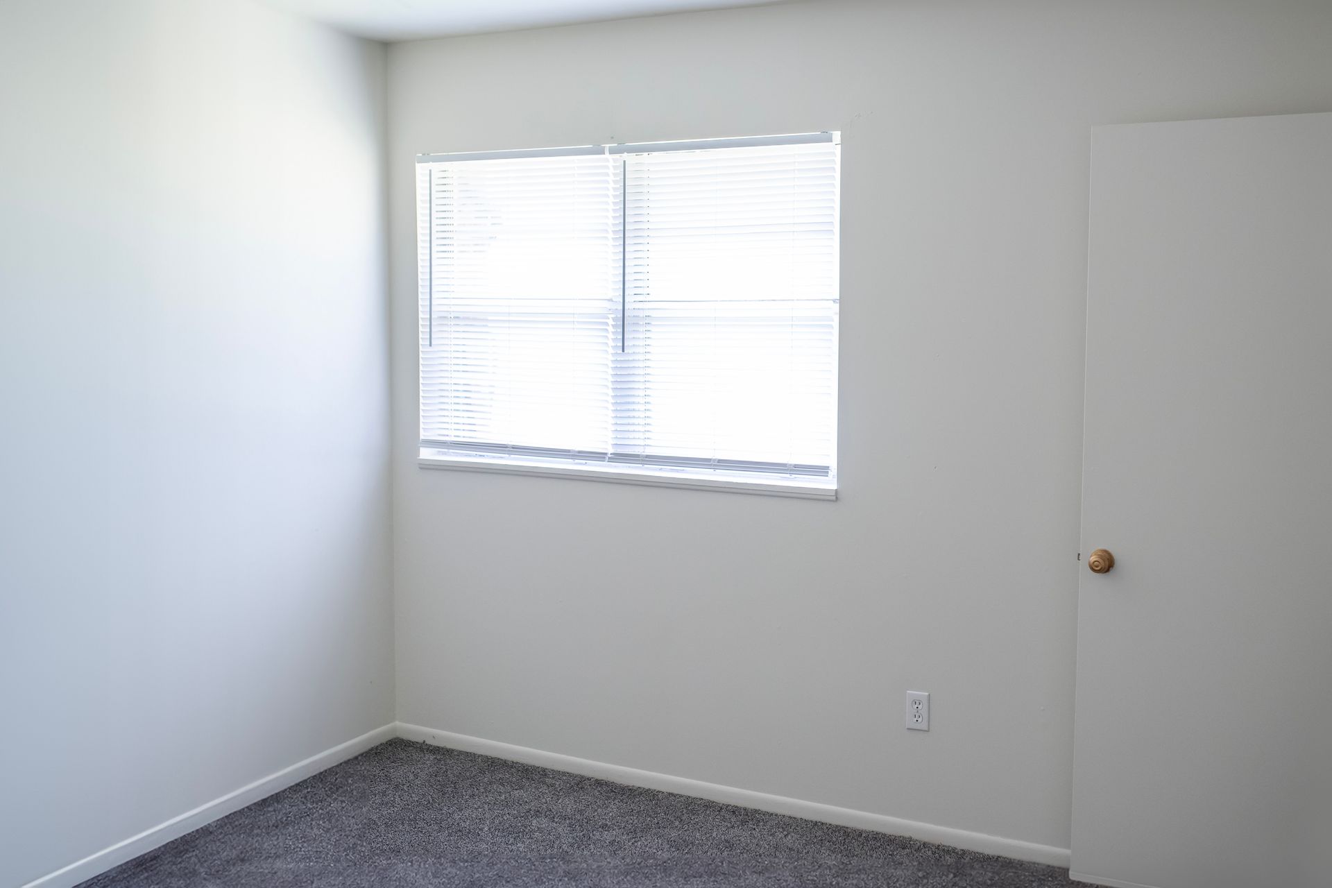 An empty bedroom with a window and a door.