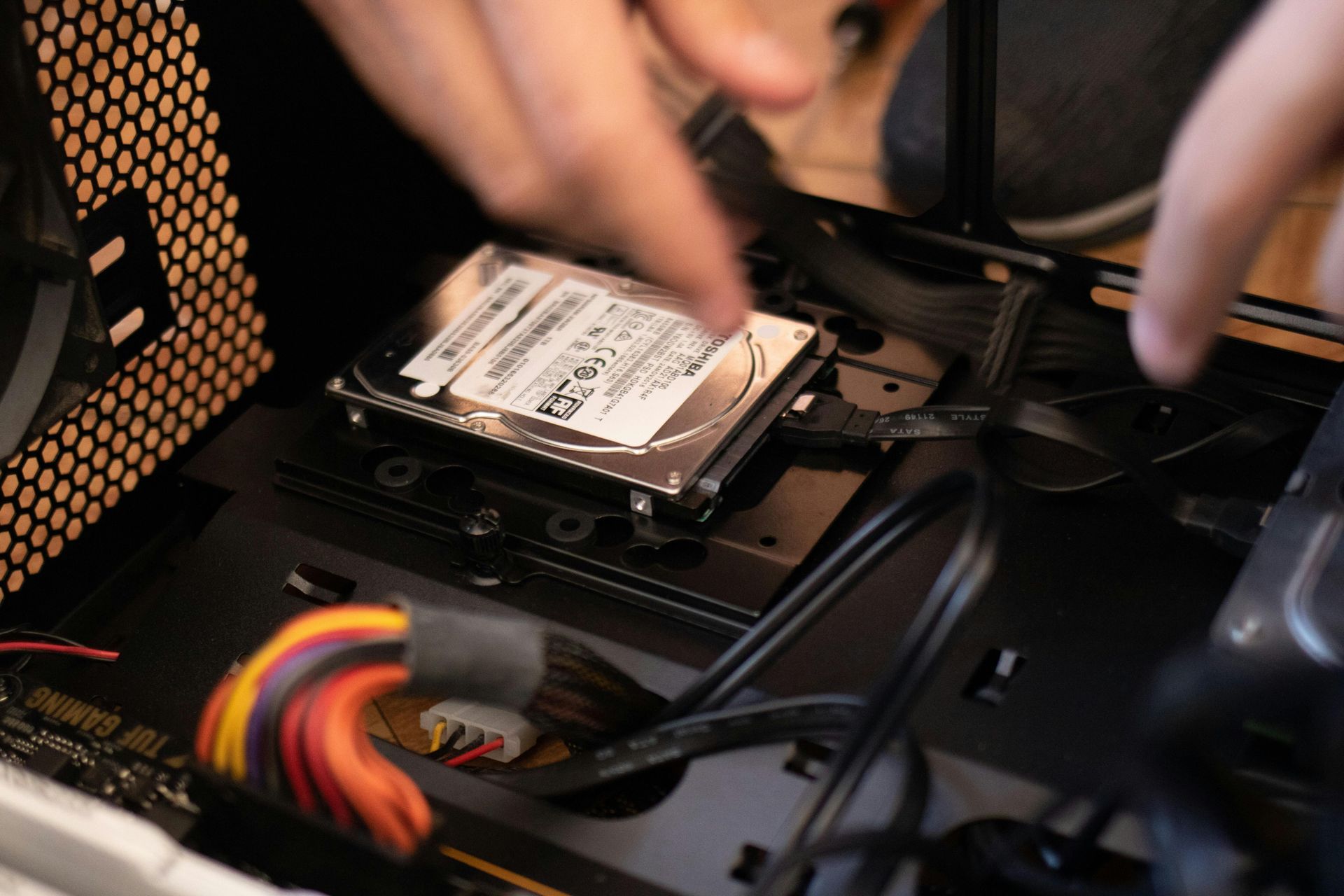 Person installs a hard drive into a computer case, with black cables and a brown side panel visible.