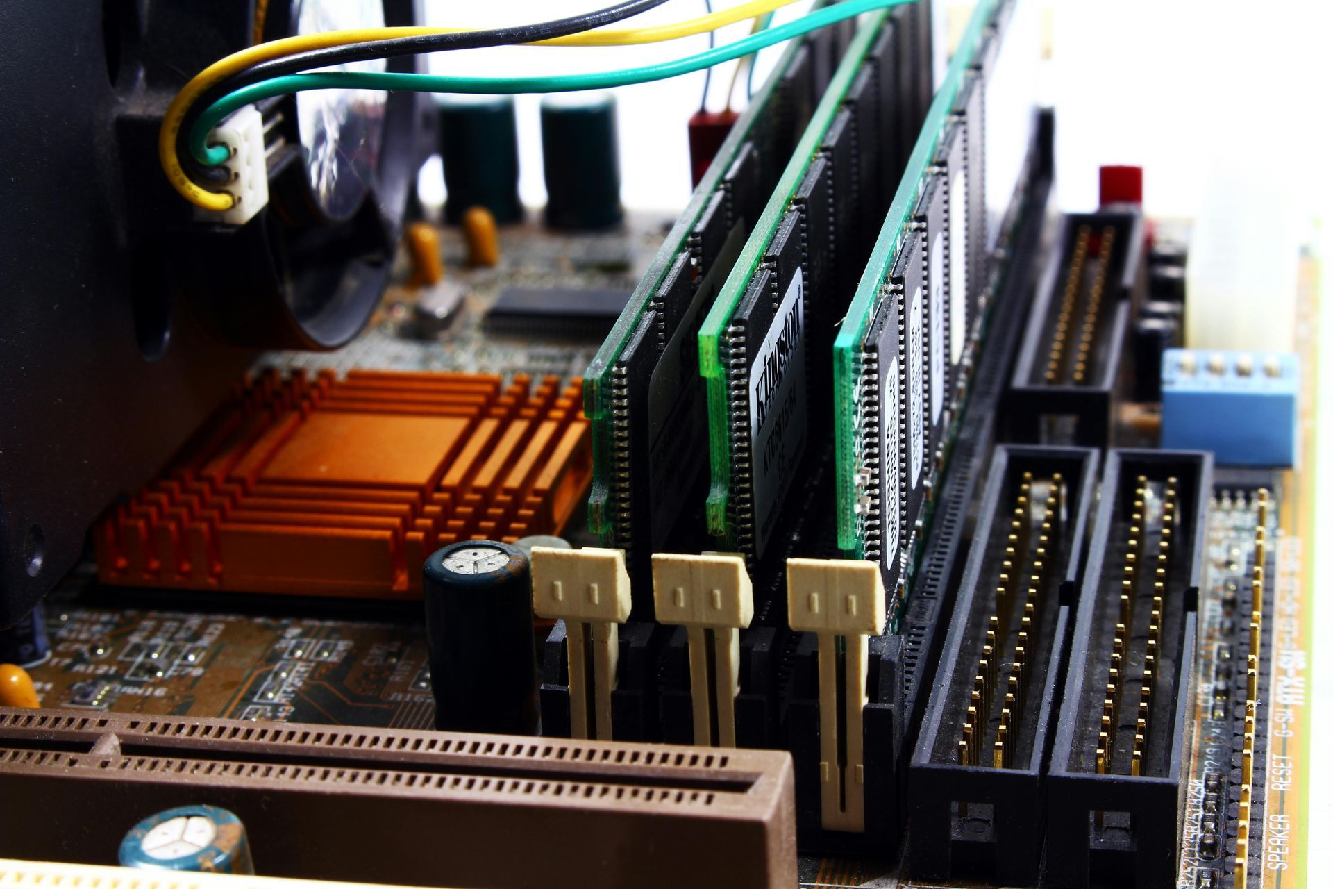 Close-up of a computer motherboard with RAM sticks installed, showing connectors, chips, and a copper heatsink.
