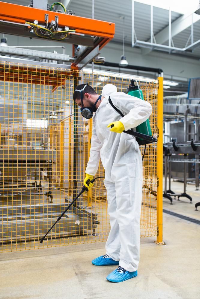 A Man In A Protective Suit Is Spraying A Machine In A Factory — X-Terminate Pest Control In Imbil, QLD
