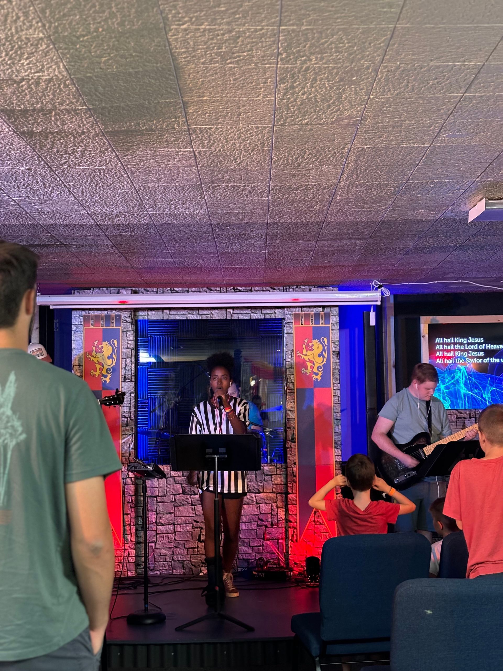 A woman is singing into a microphone on a stage while a man plays a guitar.