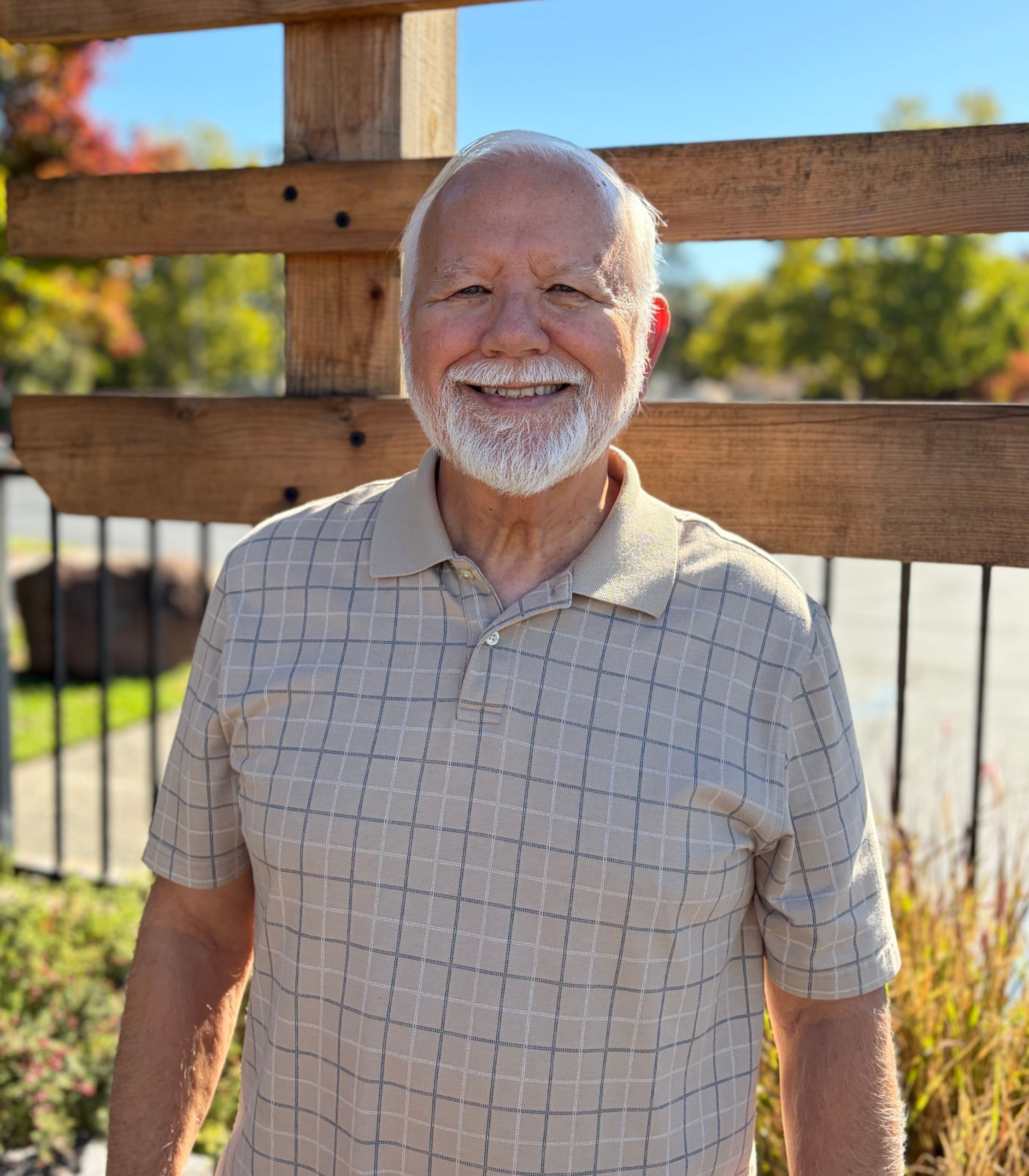 A man with long white hair and a beard is wearing a black shirt and smiling.