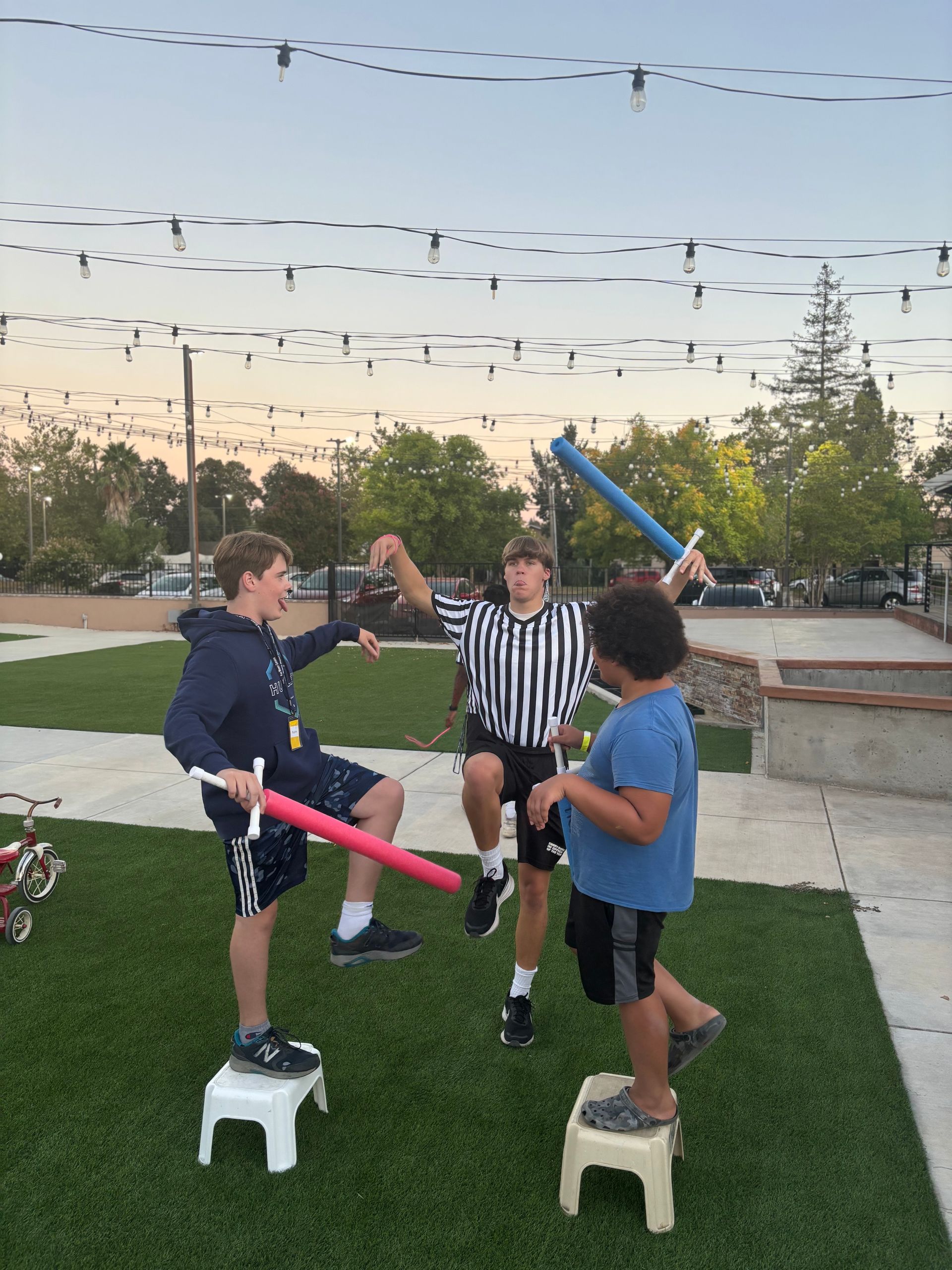 Three young boys are playing with foam swords in a park.
