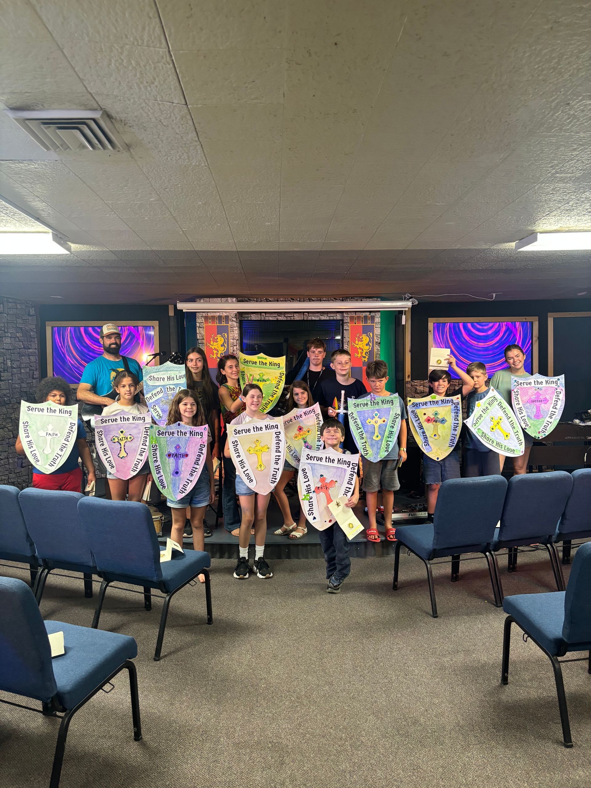 A group of children are standing in a room holding shields.