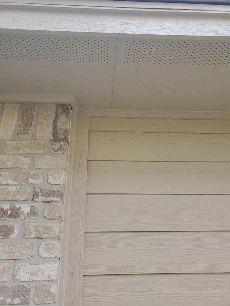 A close up of a brick wall with a white siding and a roof.
