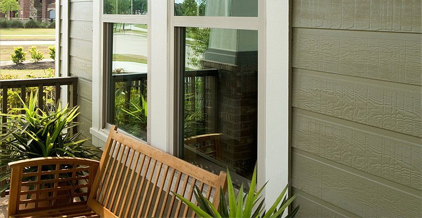 A wooden bench is sitting on the side of a house next to a window.