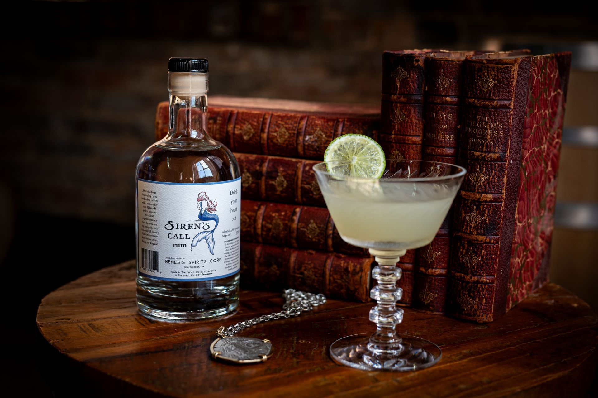 A bottle of alcohol and a glass of alcohol are on a table next to a stack of books.