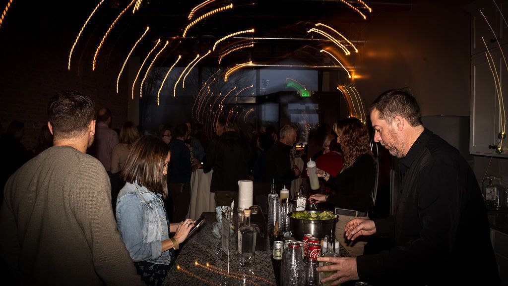 A group of people are standing around a bar in a dark room.