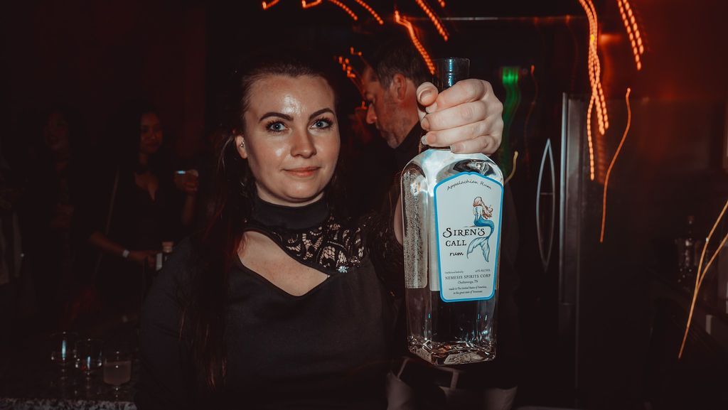 A woman is holding a bottle of alcohol in a dark room.