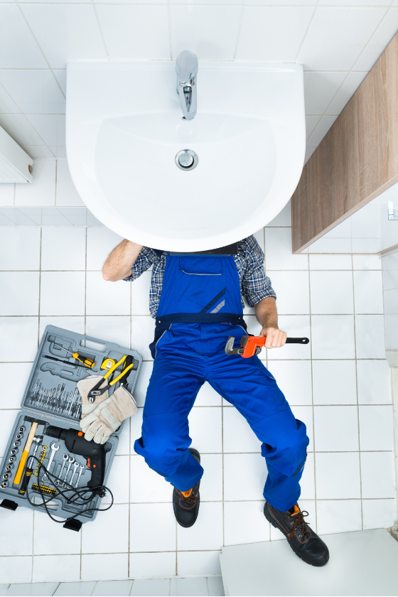 A plumber is laying on the floor under a sink in a bathroom.