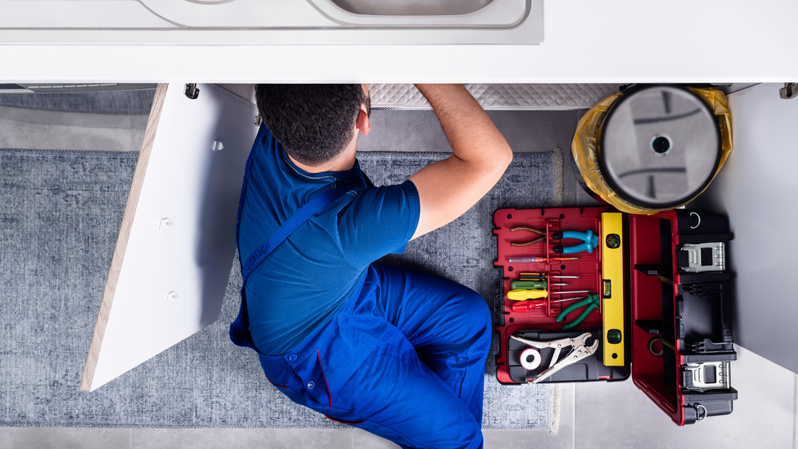 A plumber is working under a sink in a kitchen.