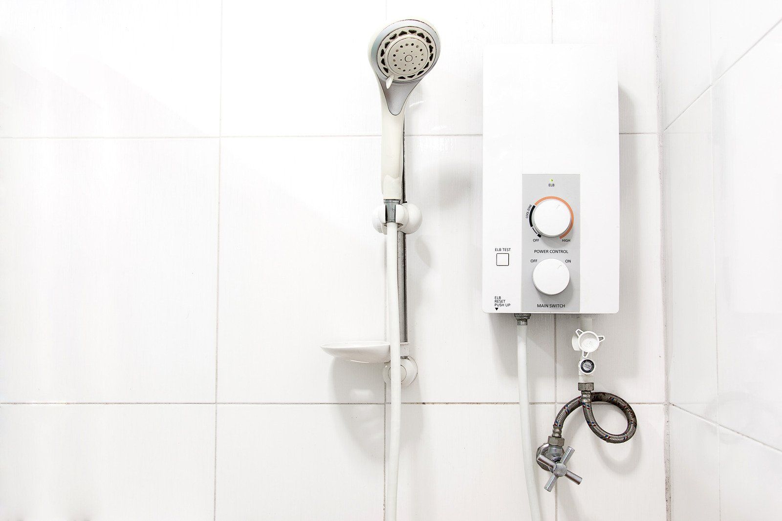 A white electric shower head and control unit mounted on white tiled wall.