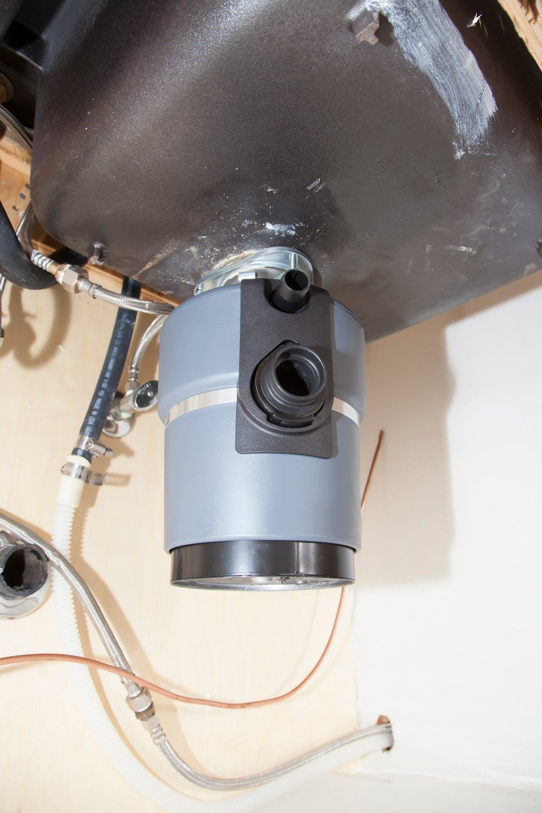 Garbage disposal unit under a sink, with pipes and wiring visible. Gray and black colors dominate.