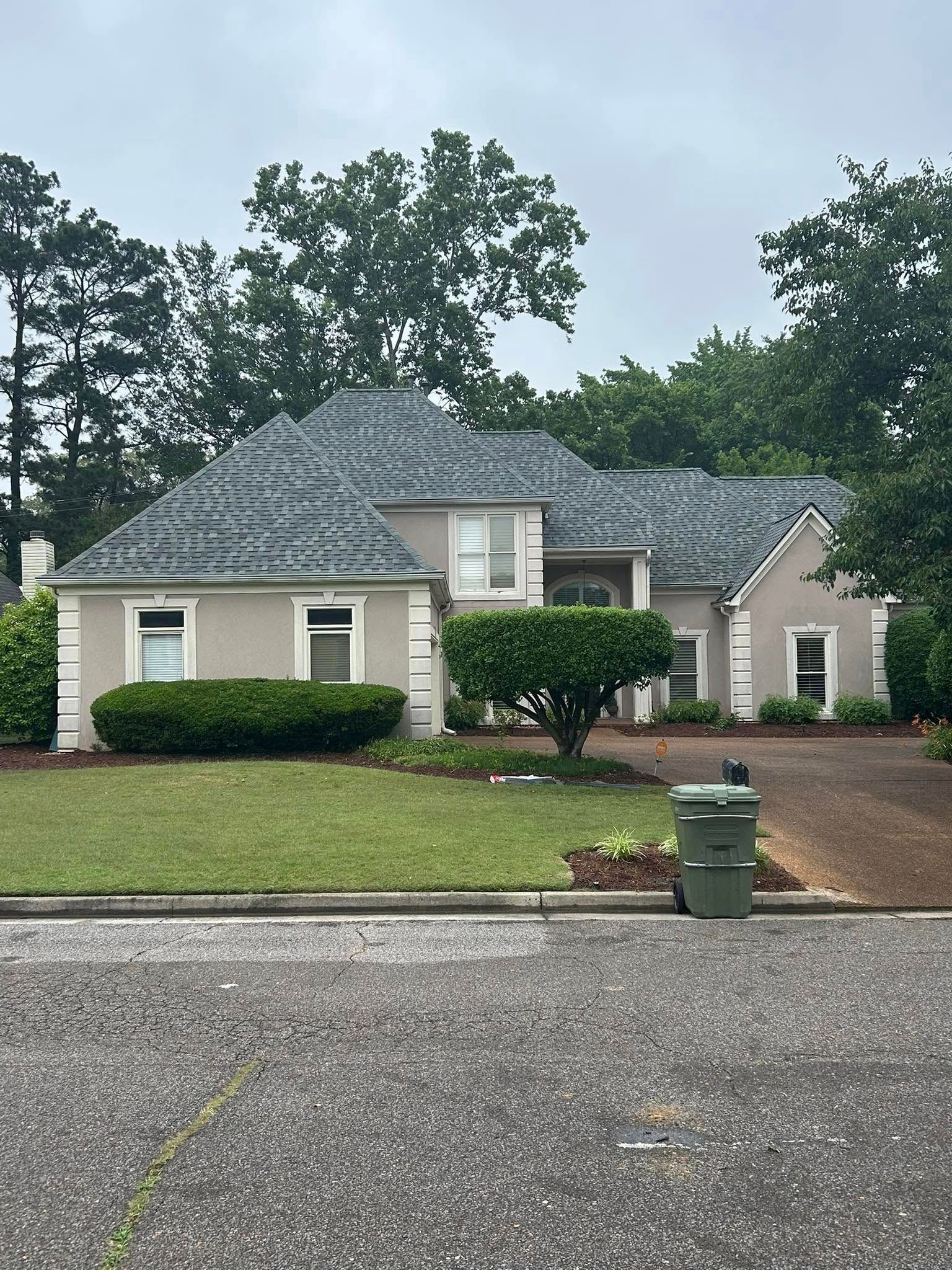 Beige house with a gray tiled roof, surrounded by greenery and trees.