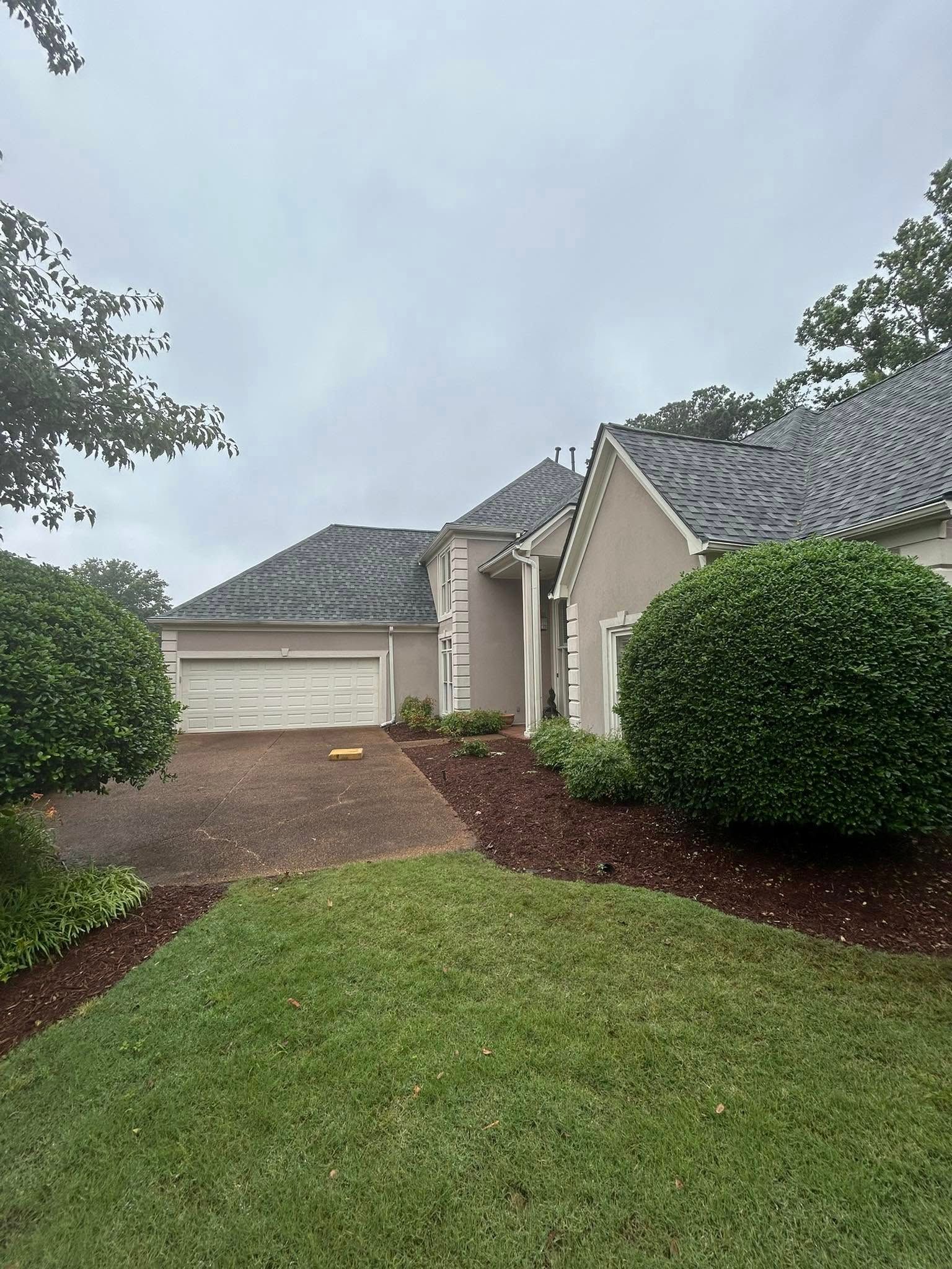 A beige house with a dark tile roof, white garage door, and green bushes.