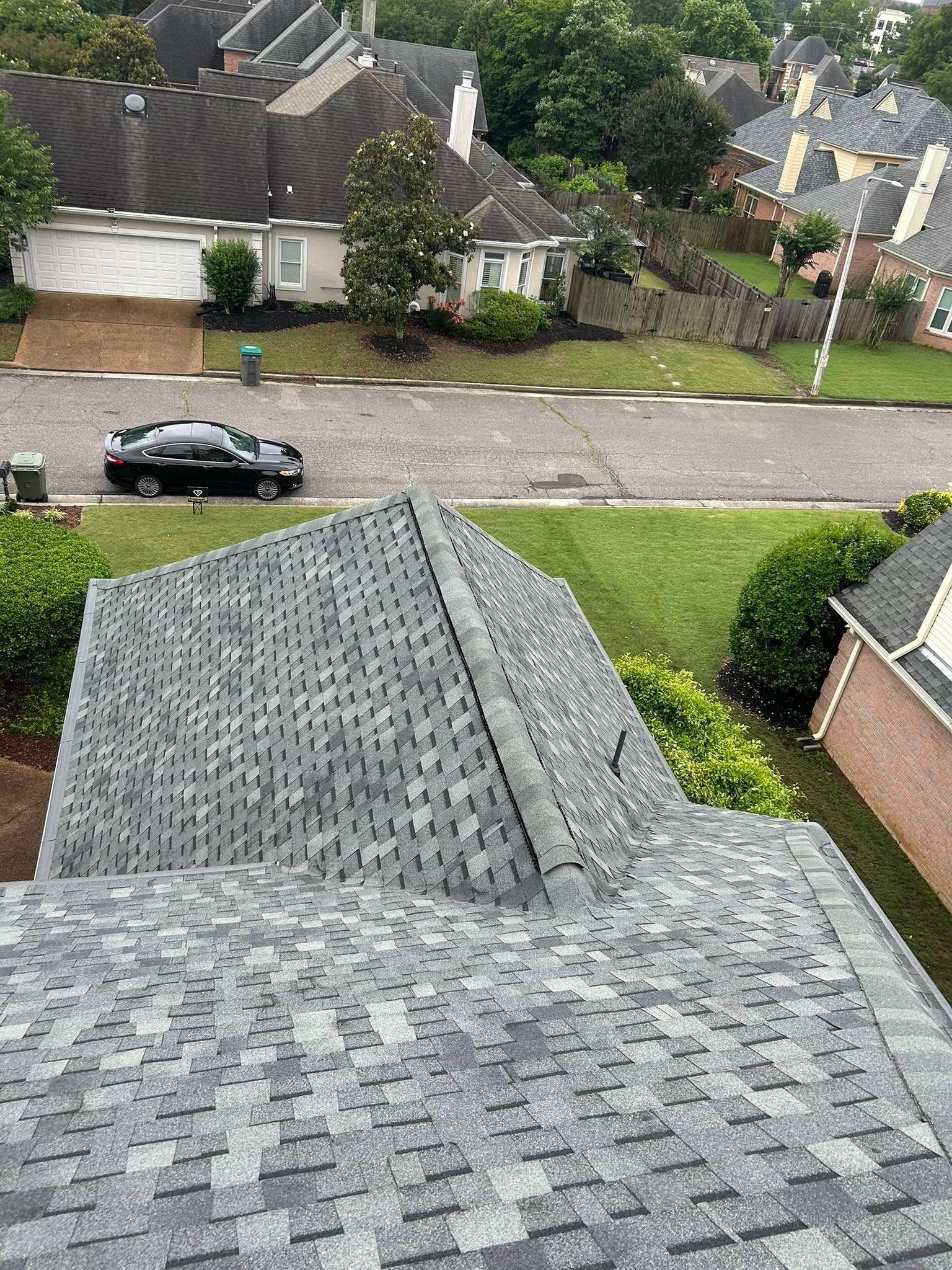 View from a roof of a suburban street lined with houses, cars parked along the road, and green lawns.
