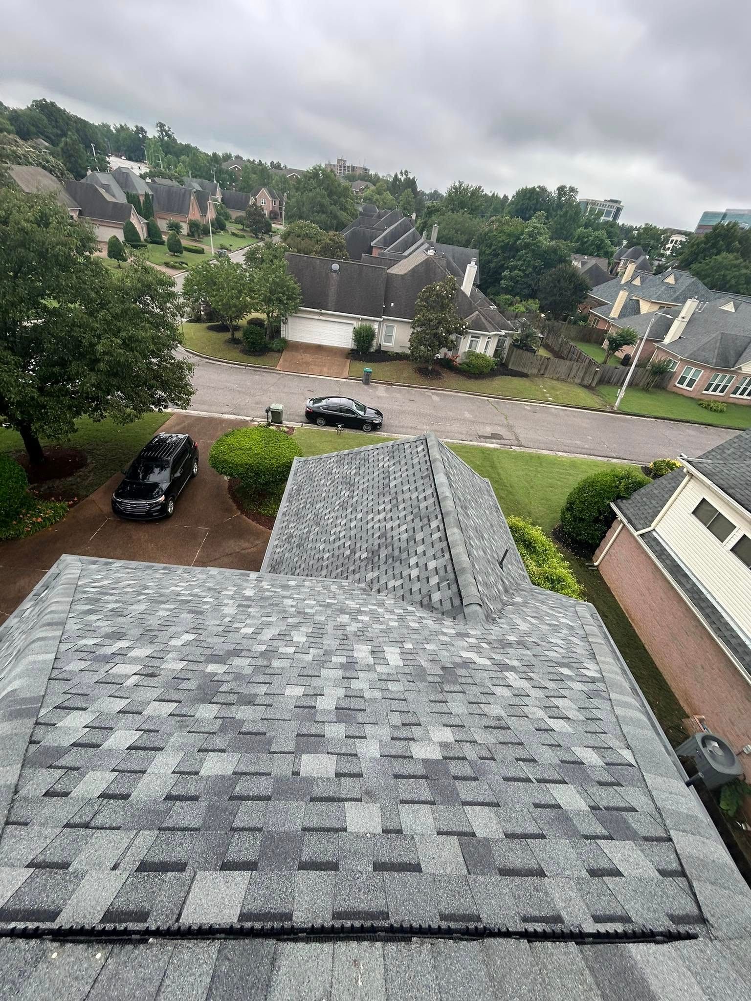 Overhead view of a house roof with gray shingles overlooking a suburban