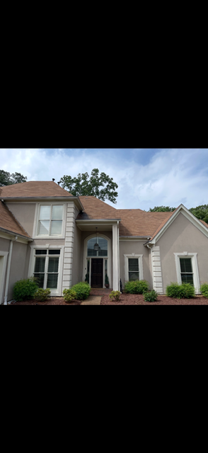 Two-story house with a green exterior, white porch, and red brick foundation.