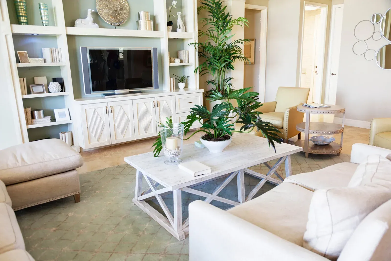Living room with white furniture, built-in TV unit, and potted plants; light and airy.