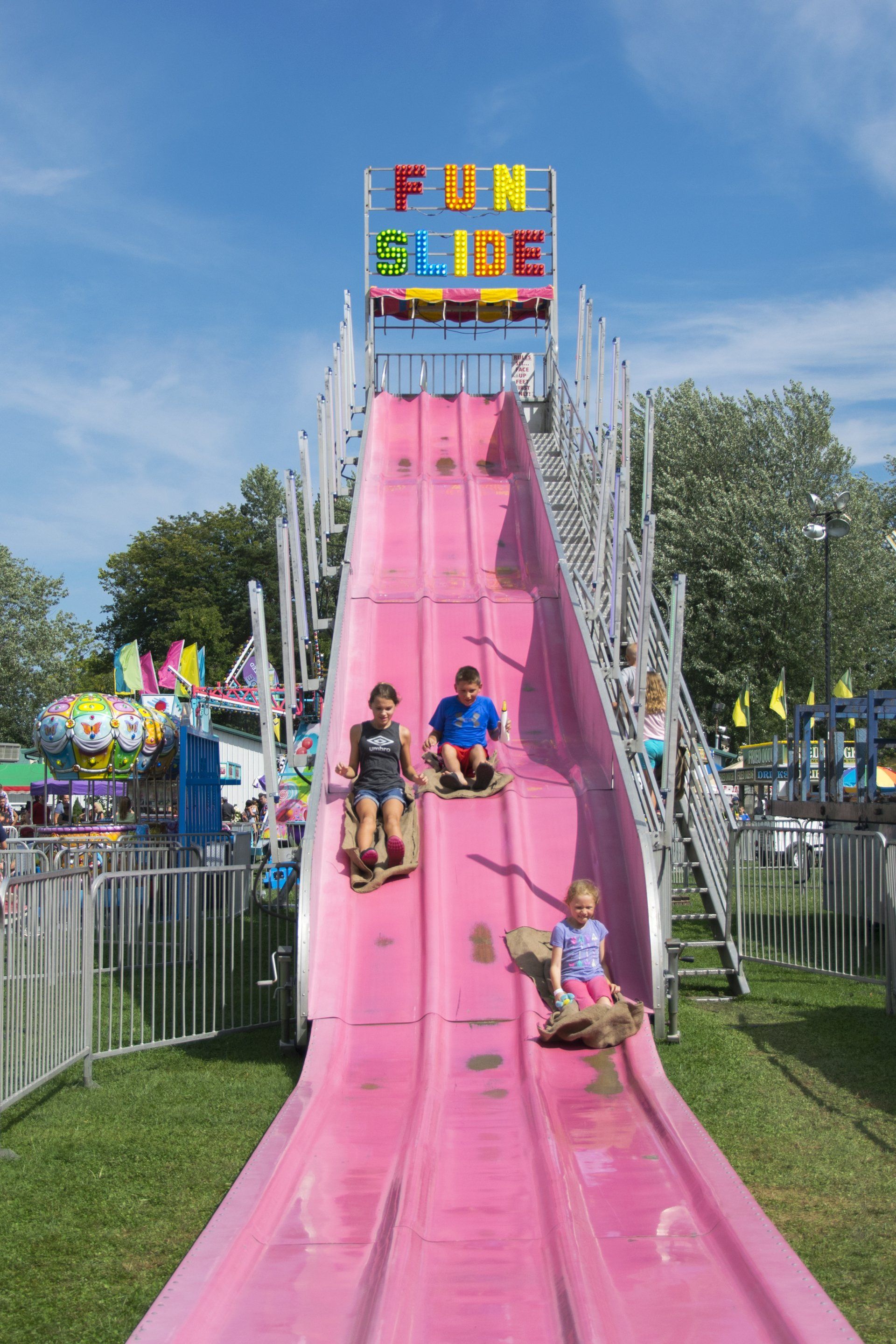 Two children are riding down a pink slide under a sign that says fun slide